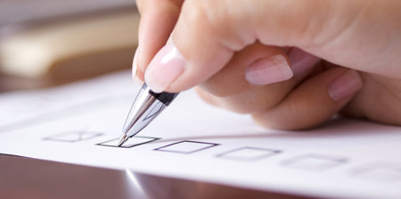 Eine Hand, die einen Stift hält und ein Kreuzchen auf einer Checkliste setzt.